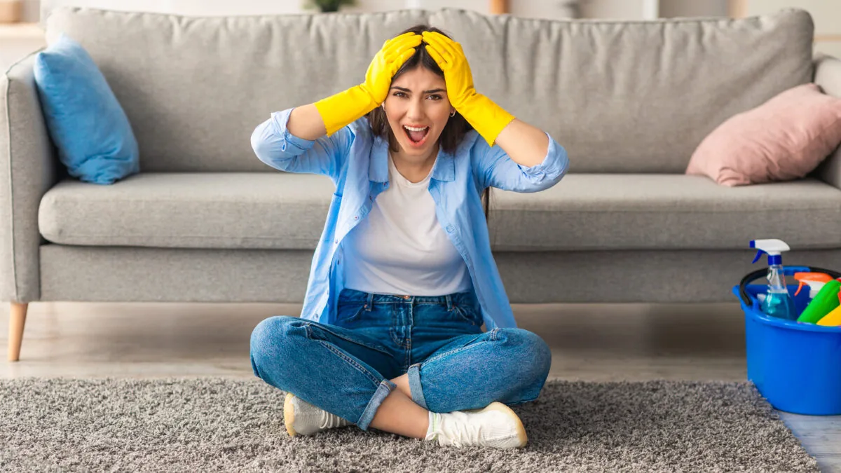 A woman in cleaning gloves sits on the floor looking frustrated and overwhelmed by her house cleaning chores ★ Prestige Carpet Cleaning Woman frustrated by carpet stains, wondering if she needs professional help instead of home carpet cleaners